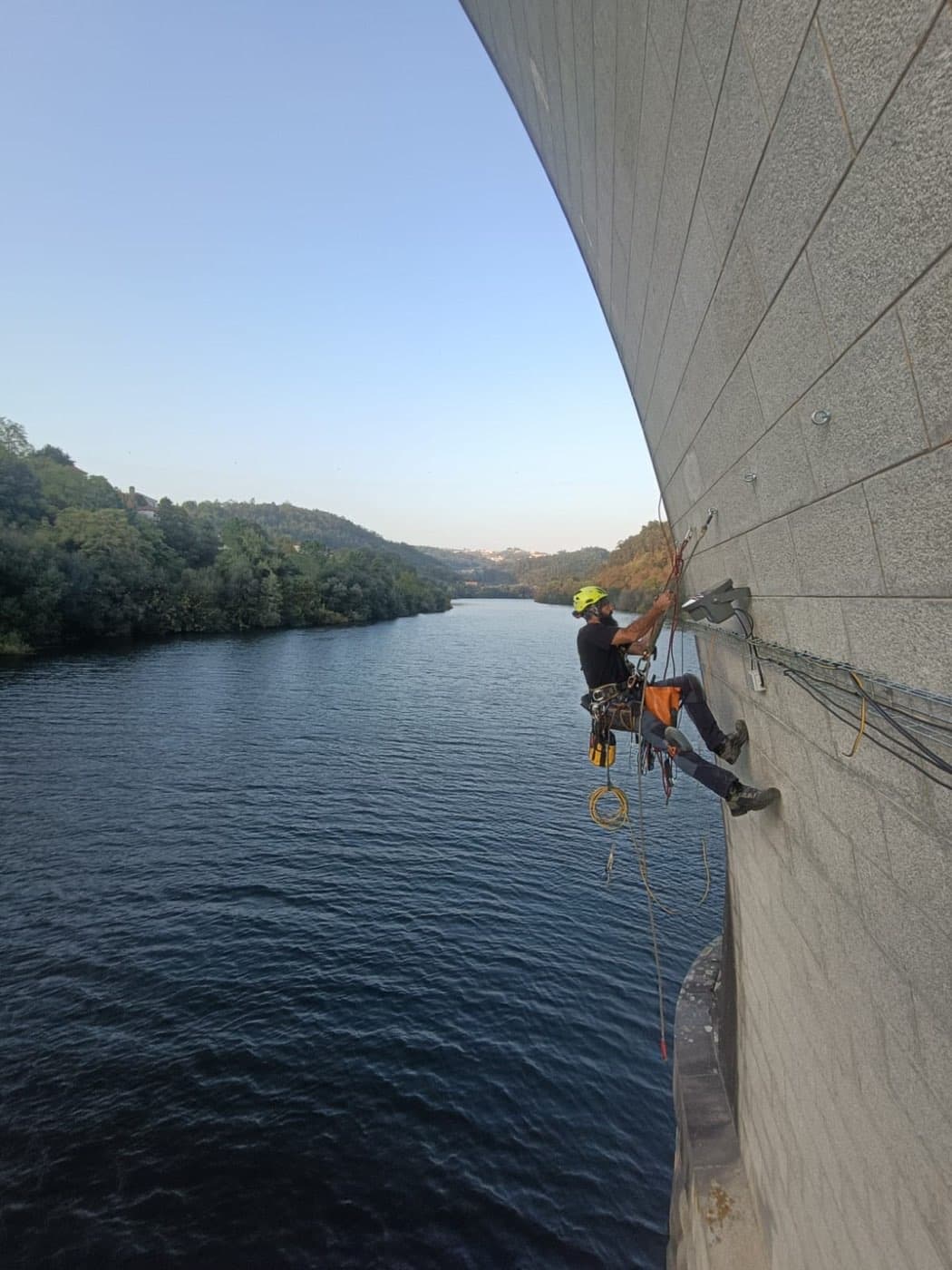 Técnico em acesso por cordas no pilar de granito da ponte sobre o rio Douro, durante a instalação.