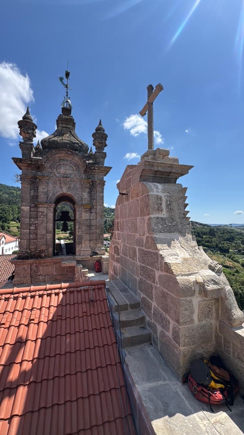 Torre sineira e cruz de pedra da igreja, alcançadas por trabalhos em altura.